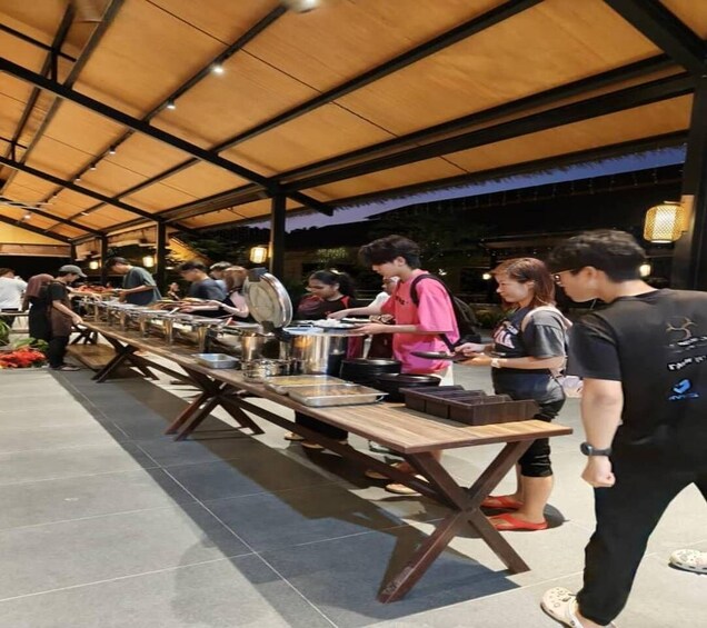 A covered outdoor dining area with long tables, people serving food, and a sunset in the background. 2