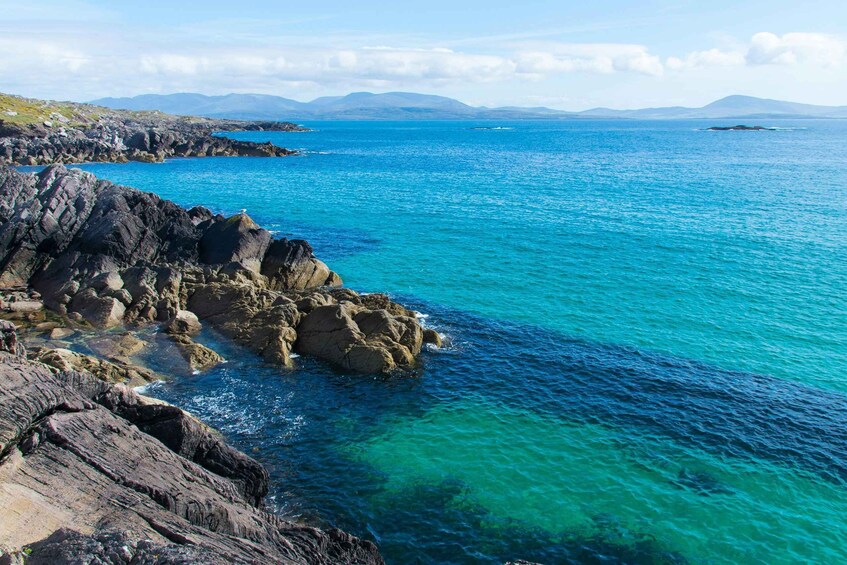 A coastal landscape with clear blue waters, rocky shores, and distant mountains. 2