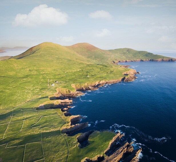 A coastal landscape with green fields, rocky cliffs, and a clear blue sea. 3