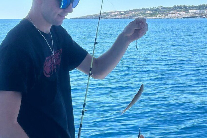 A person holding a fishing rod over a body of water with a coastline in the background. 3