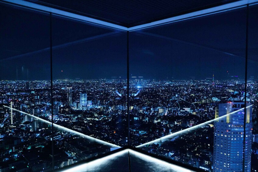 A nighttime cityscape viewed through a glass structure with illuminated lines. 1