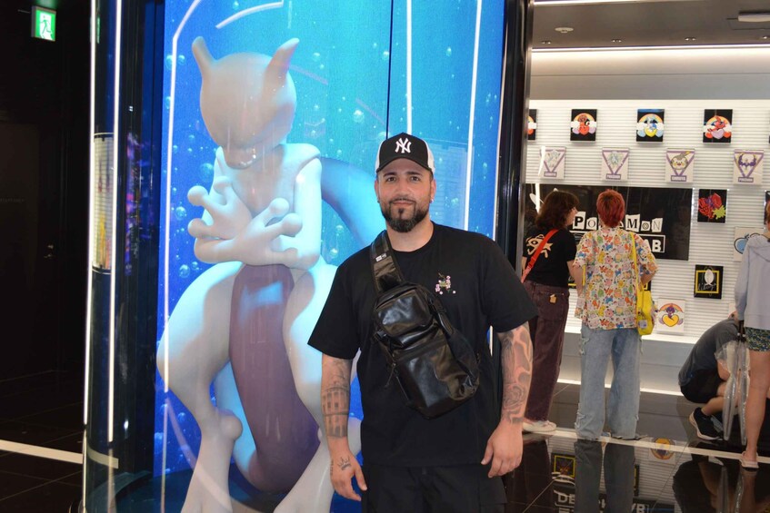 A man standing in front of a large digital display with a character, and a wall with various Pokémon-themed items. 2