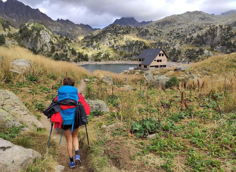 A hiker on a trail with a mountain backdrop and a house by a lake. 4