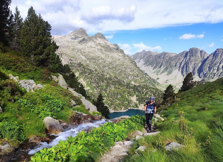 A hiker on a mountain trail with a lake and rocky mountains in the background. 3