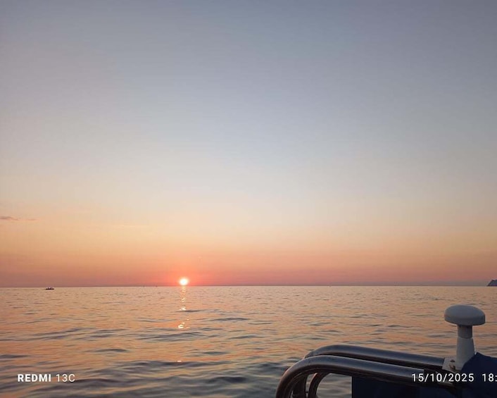 A sunset over calm waters with a boat's railing in the foreground. 5