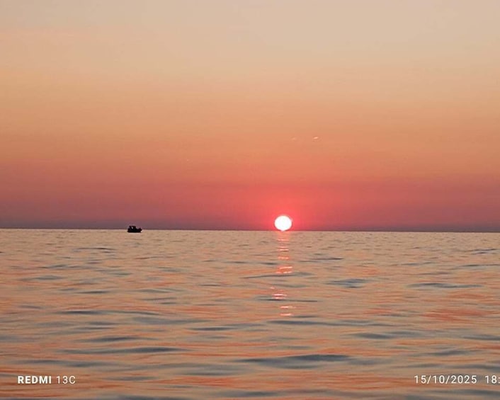 A sunset over a calm sea with a boat in the distance. 1