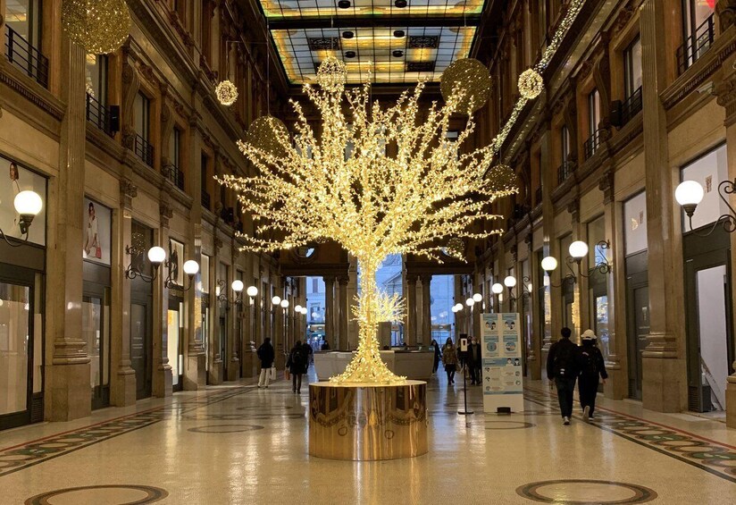 A grand indoor space with a large illuminated tree sculpture at the center, surrounded by columns and ornate lighting fixtures. 3