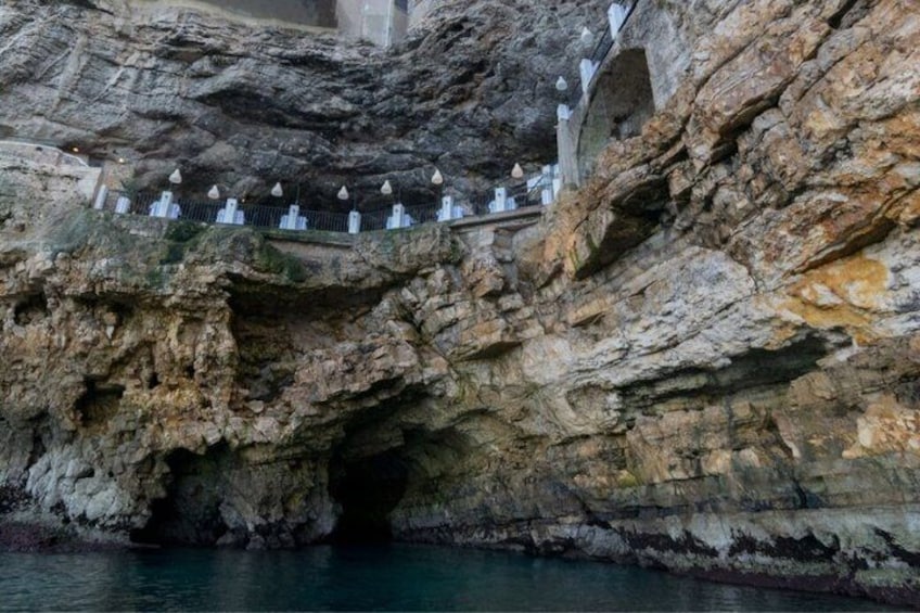 A rock formation with a cave entrance and a series of white structures on top. 5