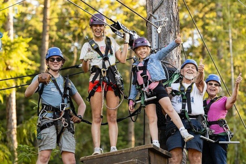 People on a zip line course, wearing helmets and harnesses, in a forested area. 4