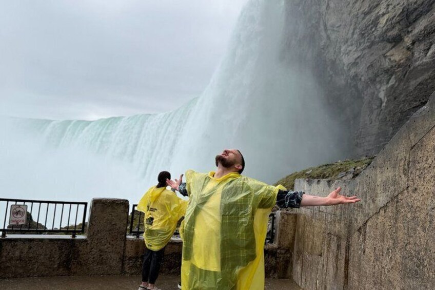 A person in a yellow raincoat standing with arms outstretched, facing a waterfall. 1