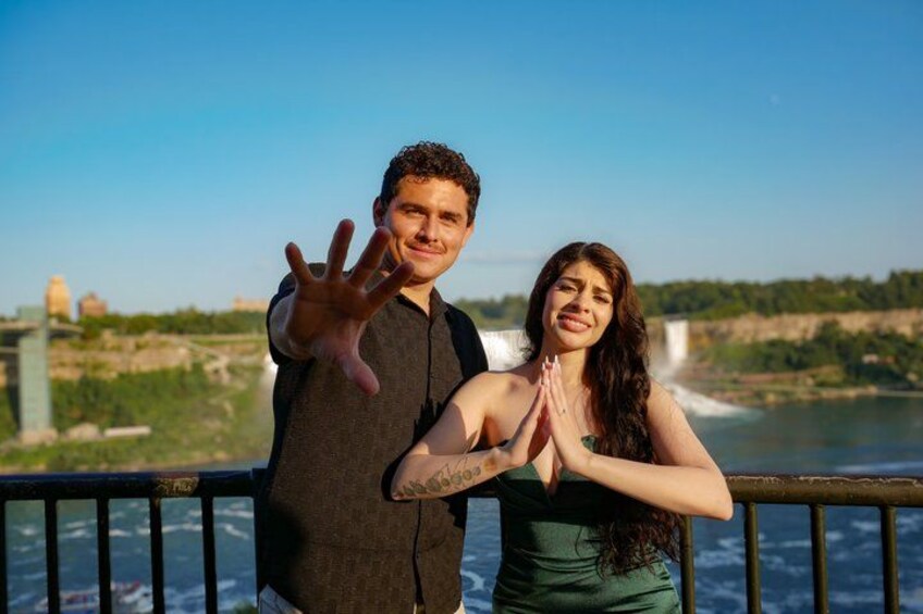 A man and a woman standing by a railing with a river and a bridge in the background. 2