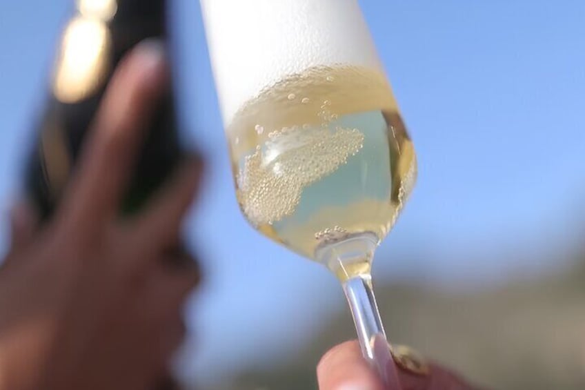 A hand holding a glass with a clear liquid, possibly a drink, against a blurred background. 1