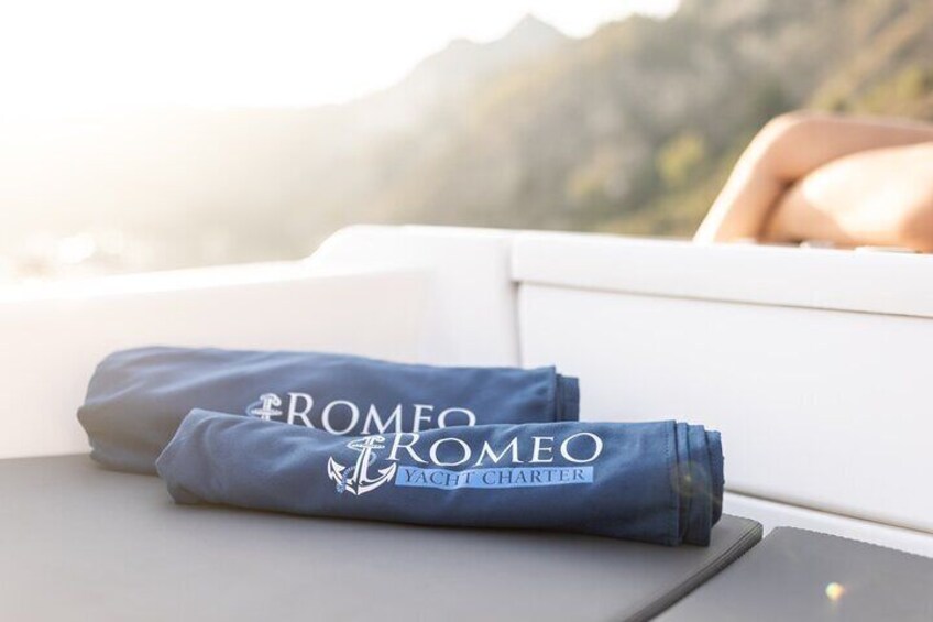 A folded blue towel with 'ROMEO & JULIET' and 'YACHT CHARTER' text on a boat deck. 2