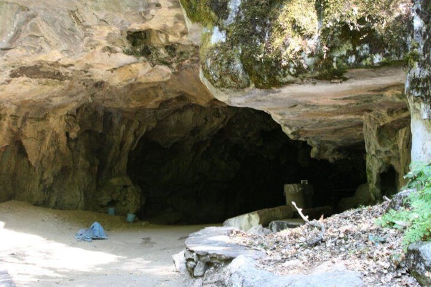 A cave entrance with a moss-covered rock overhang and a small stream flowing into the cave. 2