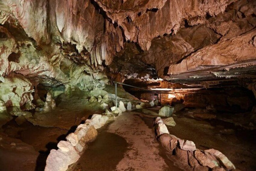 A cave with stalactites and stalagmites, a rope for safety, and a metal railing. 3