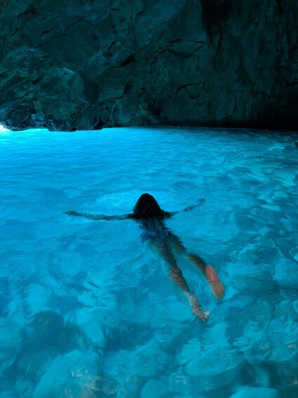 A person swimming in clear blue water with rocky cave walls in the background. 1