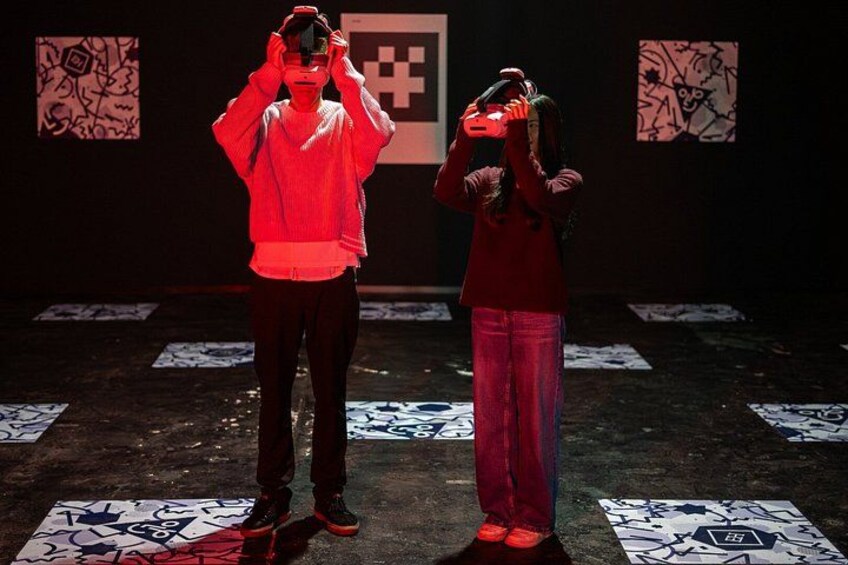 Two people in a dark room with red lighting, standing on patterned floor tiles. 3