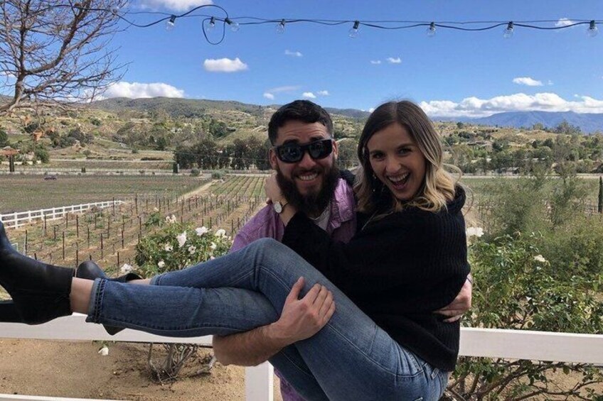 A person sitting on a railing with a vineyard in the background. 2