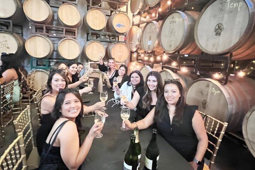 A group of people toasting with champagne in a wine cellar with wooden barrels. 3