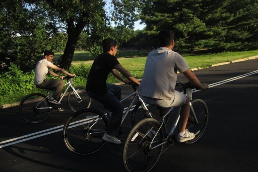 Three cyclists on a paved path in a park with trees and grass. 2