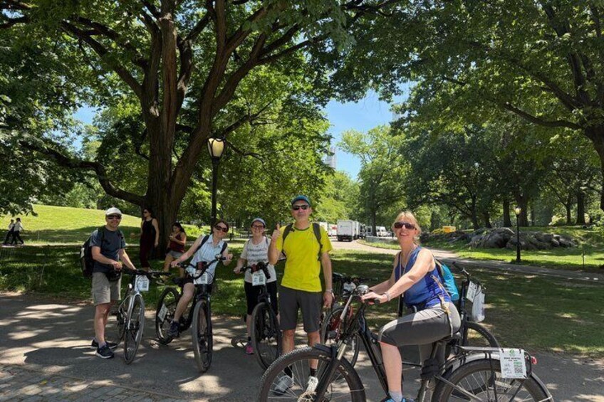 A group of people on bicycles in a park with trees and a paved path. 1