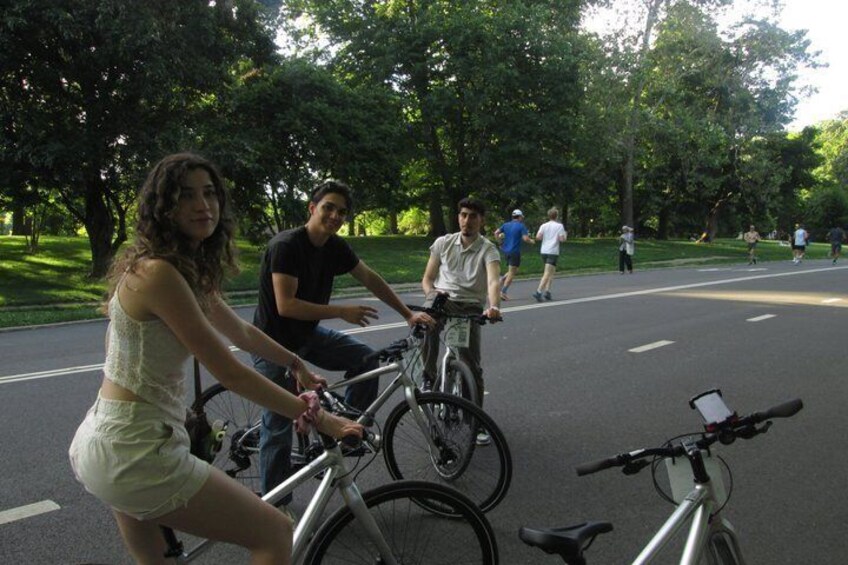 A person riding a bicycle on a road with trees and other cyclists in the background. 3
