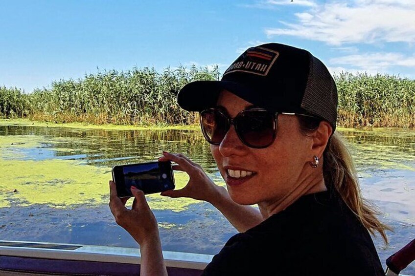A person taking a photo of a water body with vegetation in the background. 3