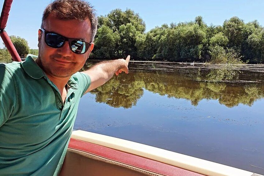 A person on a boat pointing towards a calm river with trees in the background. 2