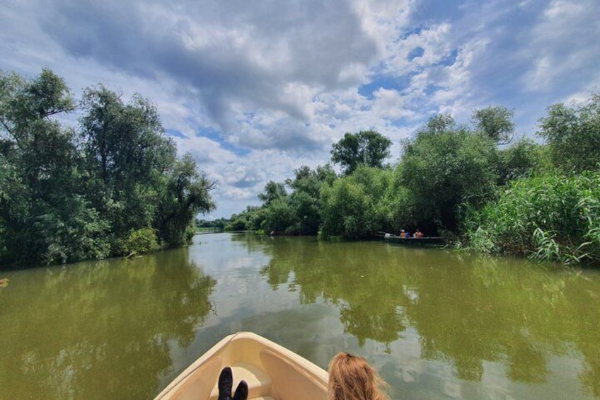 A river with dense foliage on both banks, a boat with two people, and a partly cloudy sky. 5