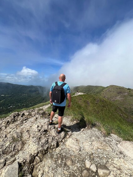 A person hiking on a rocky mountain path with a clear sky and green hills in the background. 2