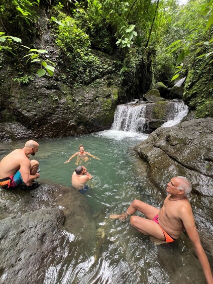 A waterfall in a forested area with people sitting and standing in the water. 3