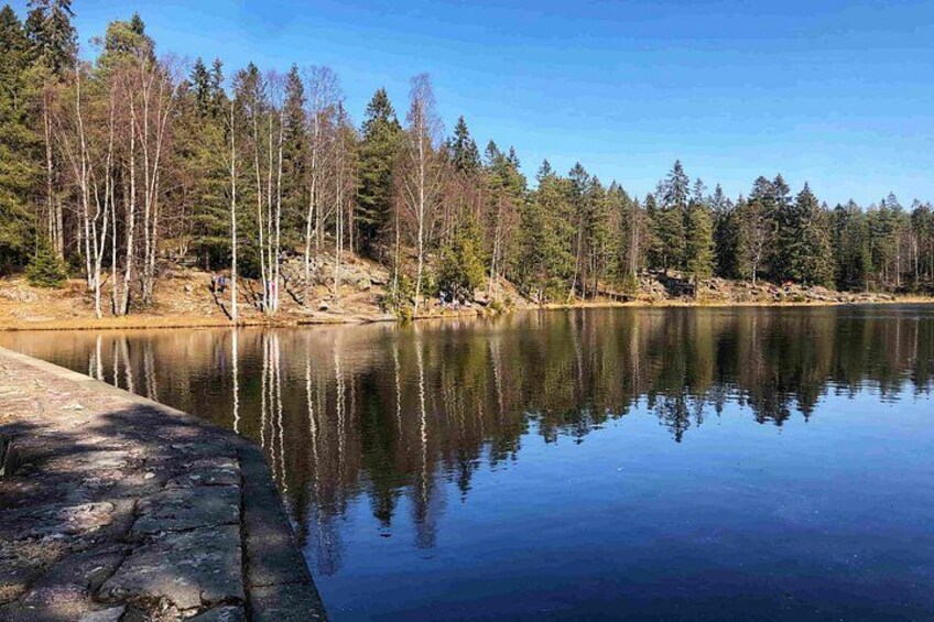 A calm lake with reflections of trees, a stone dock, and a clear blue sky. 2
