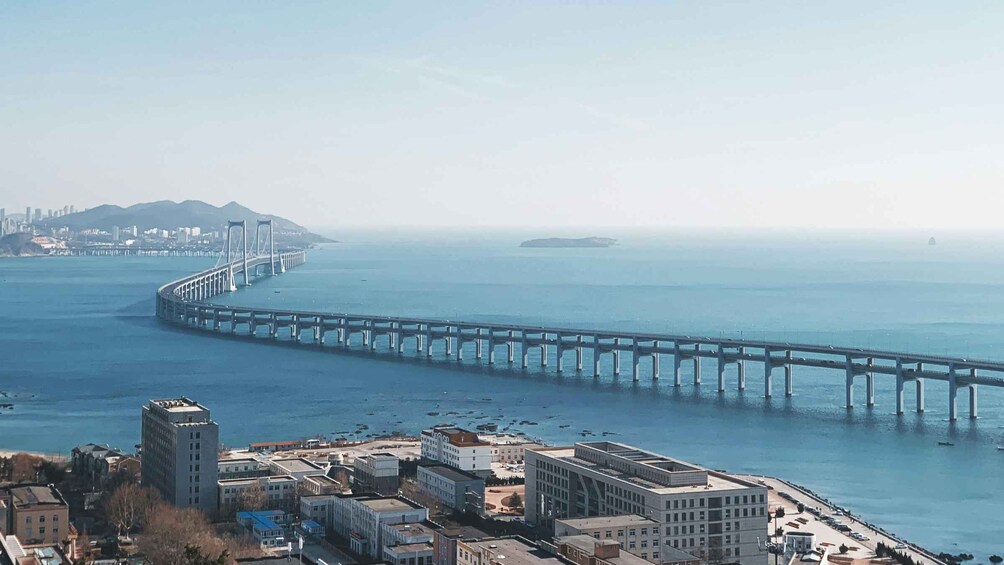 A coastal city with a prominent bridge extending into the water, a mountain range in the distance, and a dense urban area with various buildings. 1