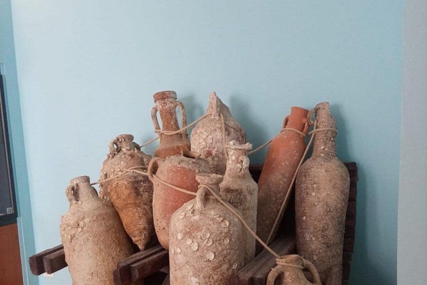 A collection of ancient terracotta pots tied together on a wooden shelf against a light blue wall. 2