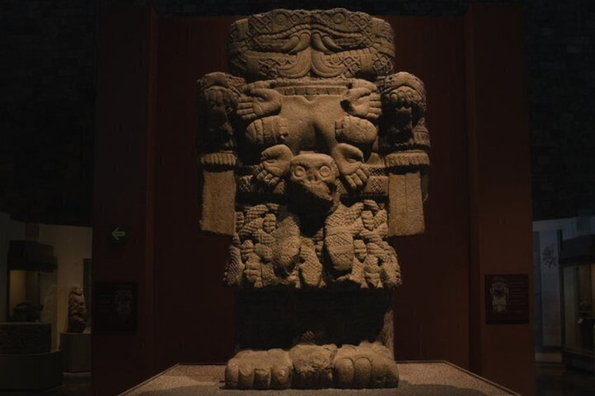 A stone sculpture with intricate carvings, including figures and patterns, displayed in a museum setting. 2