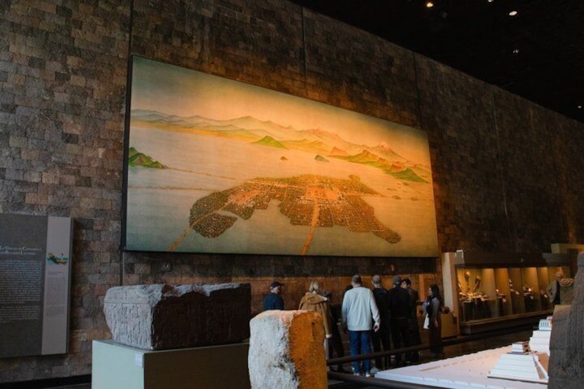A large mural of a landscape with mountains and a body of water, a brick wall, and several people observing the artwork. 5