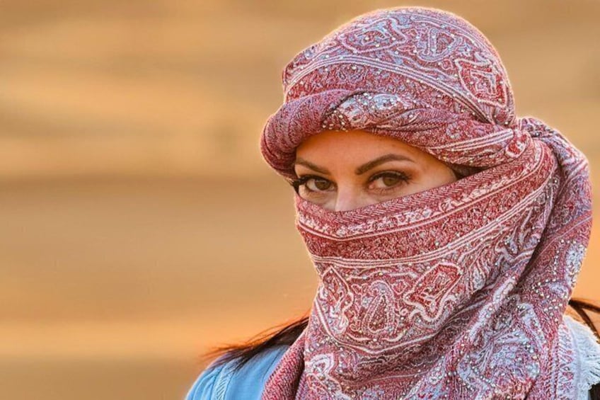 A person wearing a patterned headscarf, standing in a desert landscape. 1