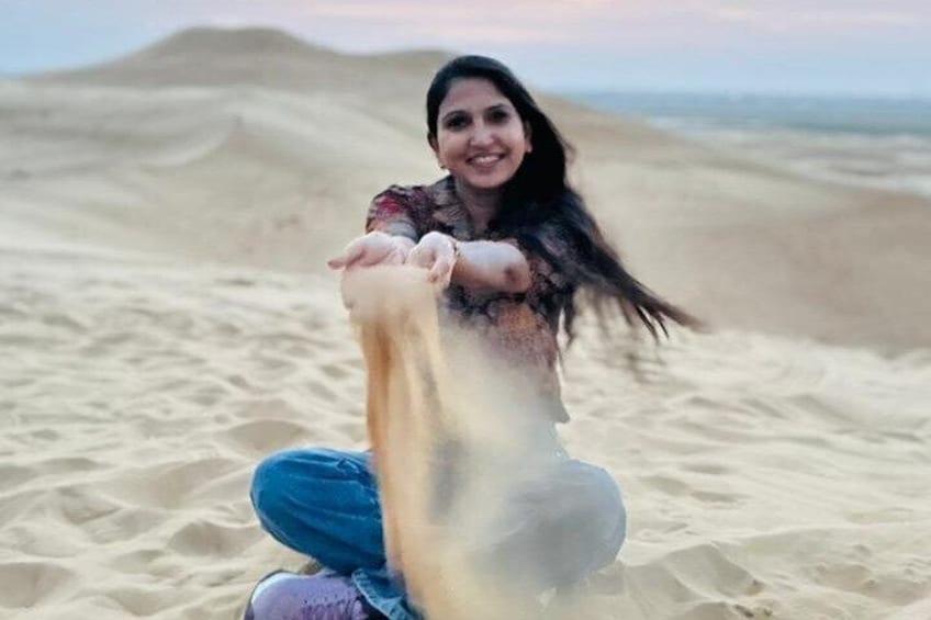 A person kneeling on a sandy beach, holding a large amount of sand. 3