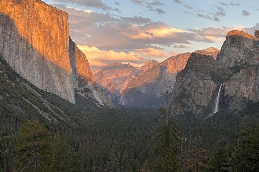 A canyon with a waterfall, steep cliffs, and a forested valley. 1