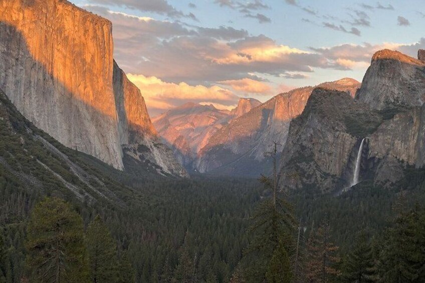 A canyon with a waterfall, steep cliffs, and a forested valley. 1