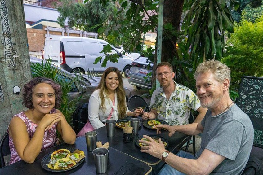 Four people dining outdoors at a table with food and drinks. 3