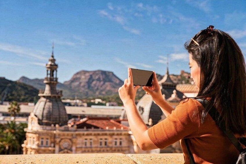 A person taking a photo of a historic building with domes and a mountain in the background. 3