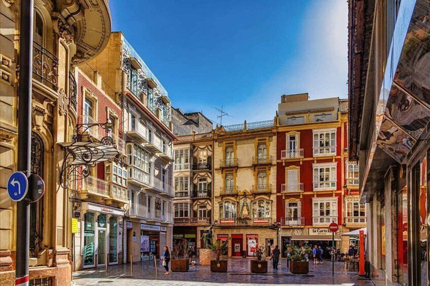 A historic European street with ornate buildings, a clear blue sky, and a pedestrian area. 2