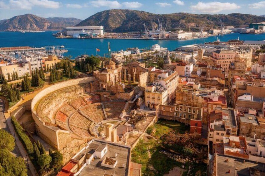 An ancient amphitheater surrounded by historic buildings and a coastal cityscape. 1