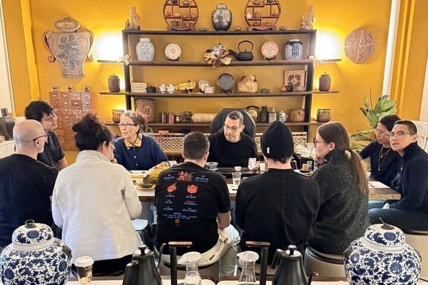 A group of people seated around a table in a room with shelves of pottery and decorative items. 5