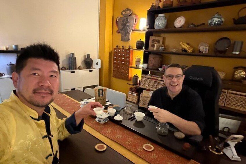 Two people sitting at a table with teacups and saucers, surrounded by shelves with various ceramic items. 1