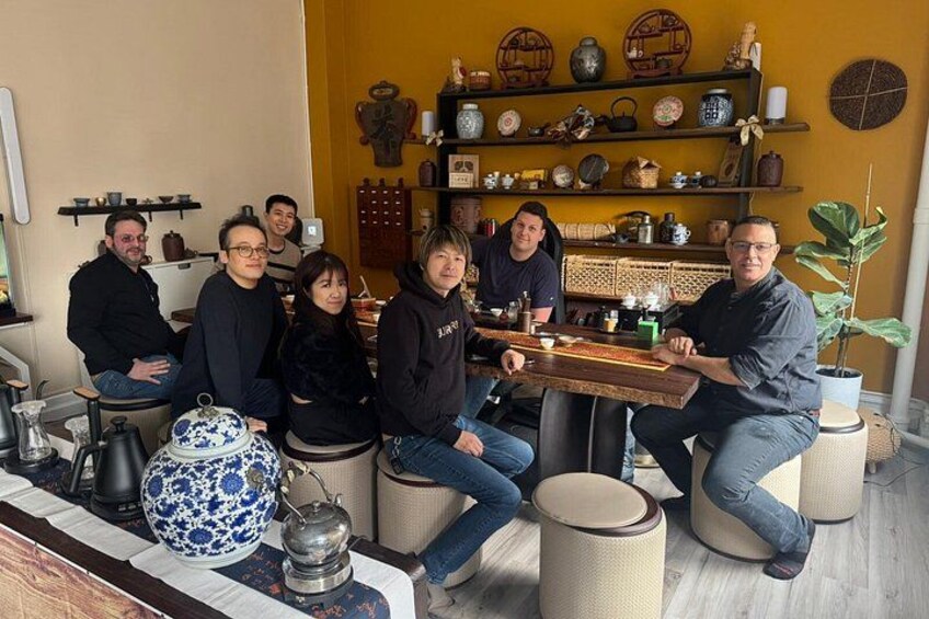 A group of people seated around a wooden table in a room with shelves of decorative items. 4