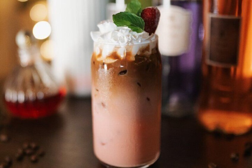 A beverage in a tall glass with whipped cream, a strawberry, and mint garnish. 1