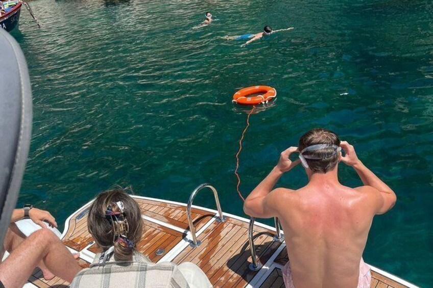 A boat with people on deck, a lifebuoy, and swimmers in the water. 3