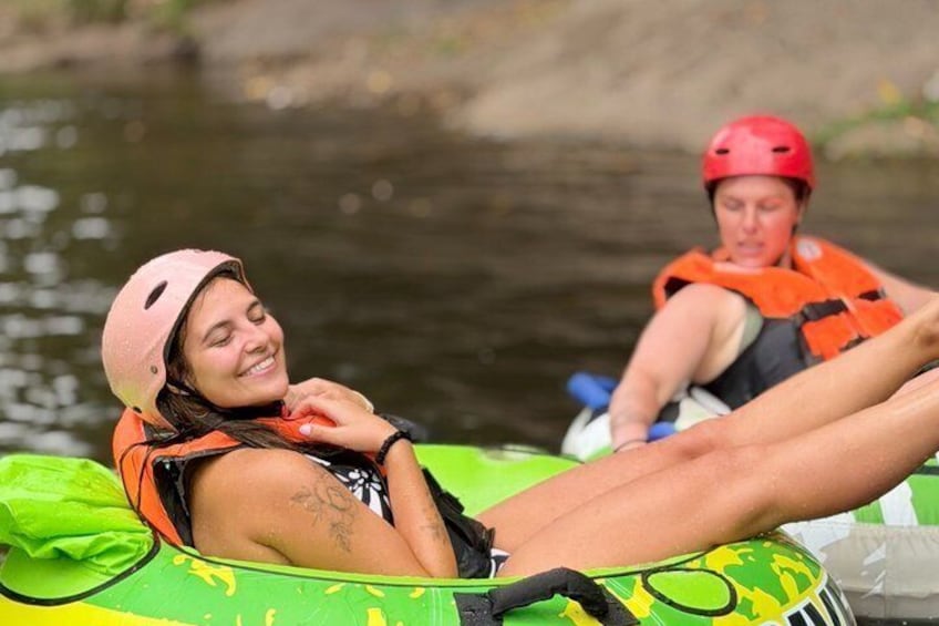 Two people in a green inflatable raft on a river, wearing helmets and life jackets. 1